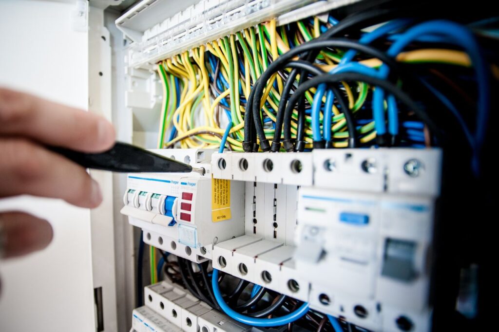 Electrician testing circuit breakers in a wiring panel with color coded wires