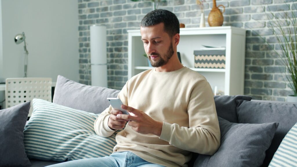Homeowner scrolling a phone on the sofa, where a retargeting ad reaches someone who already visited your site