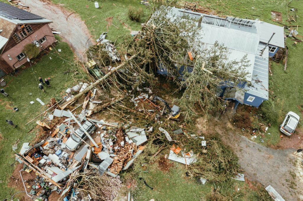 Aerial view of a home with a storm damaged roof and debris across the yard